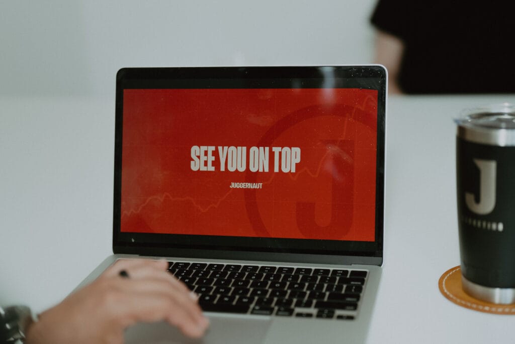 Juggernaut laptop displaying See You On Top beside a branded mug